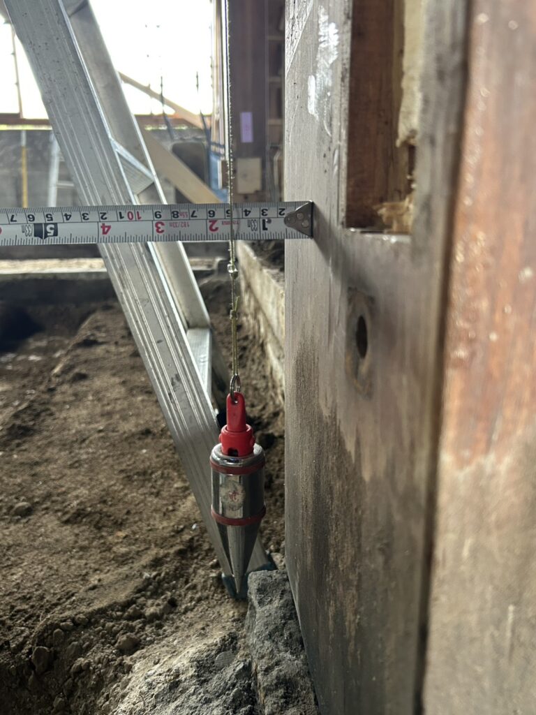 傾いた柱をまっすぐに戻すため、下げ振りで垂直を確認している様子